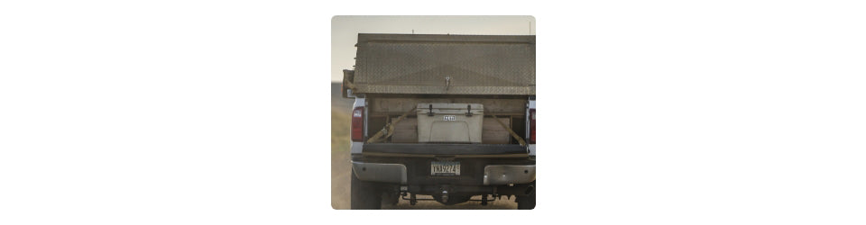 YETI cooler on the back of a pickup truck with a cargo bed cover and cooler in a desert setting