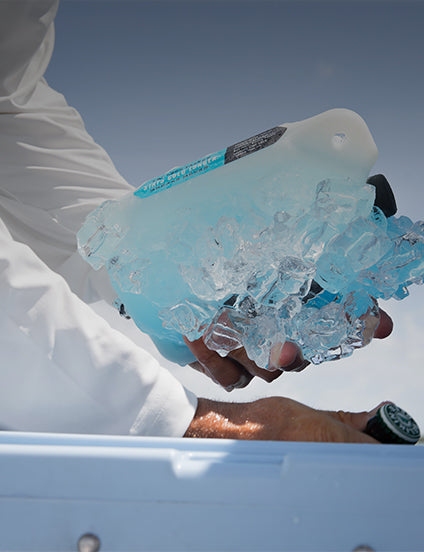 Person holding a YETI ice block  against a clear blue sky.