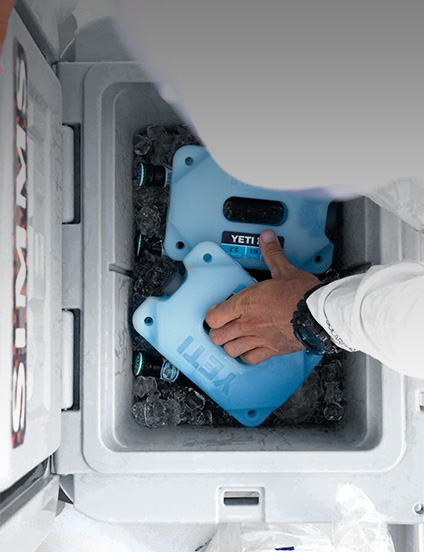 Person placing blue YETI ice blocks into a white cooler.