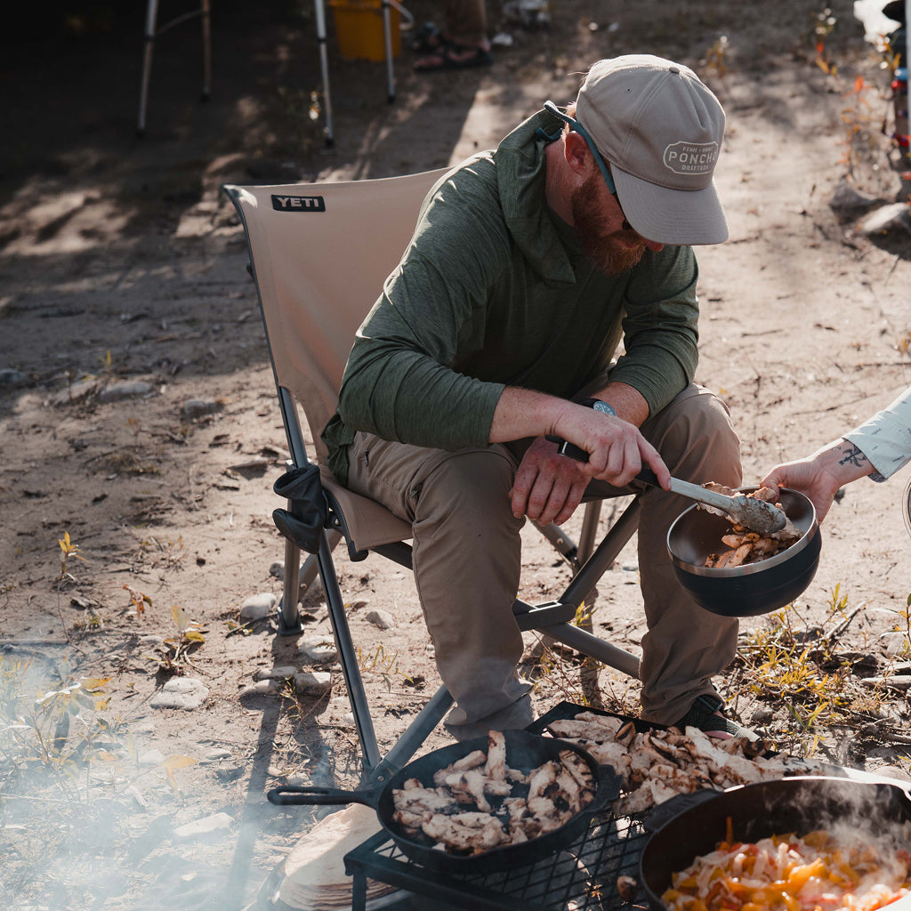 Man cooking outdoors on a camping stove with a YETI Field Chair.