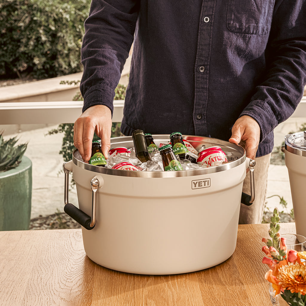 Person opening a YETI beverage tub filled with drinks on a patio.