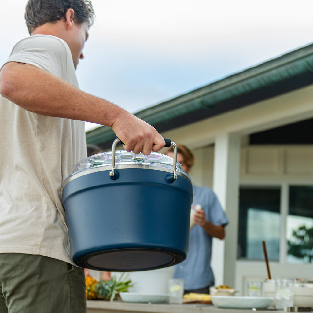 Man carrying a navy beverage tub outdoors with a blurred background