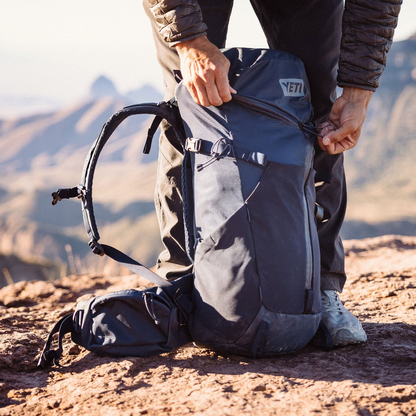 Person adjusting a backpack with a mountainous landscape in the background