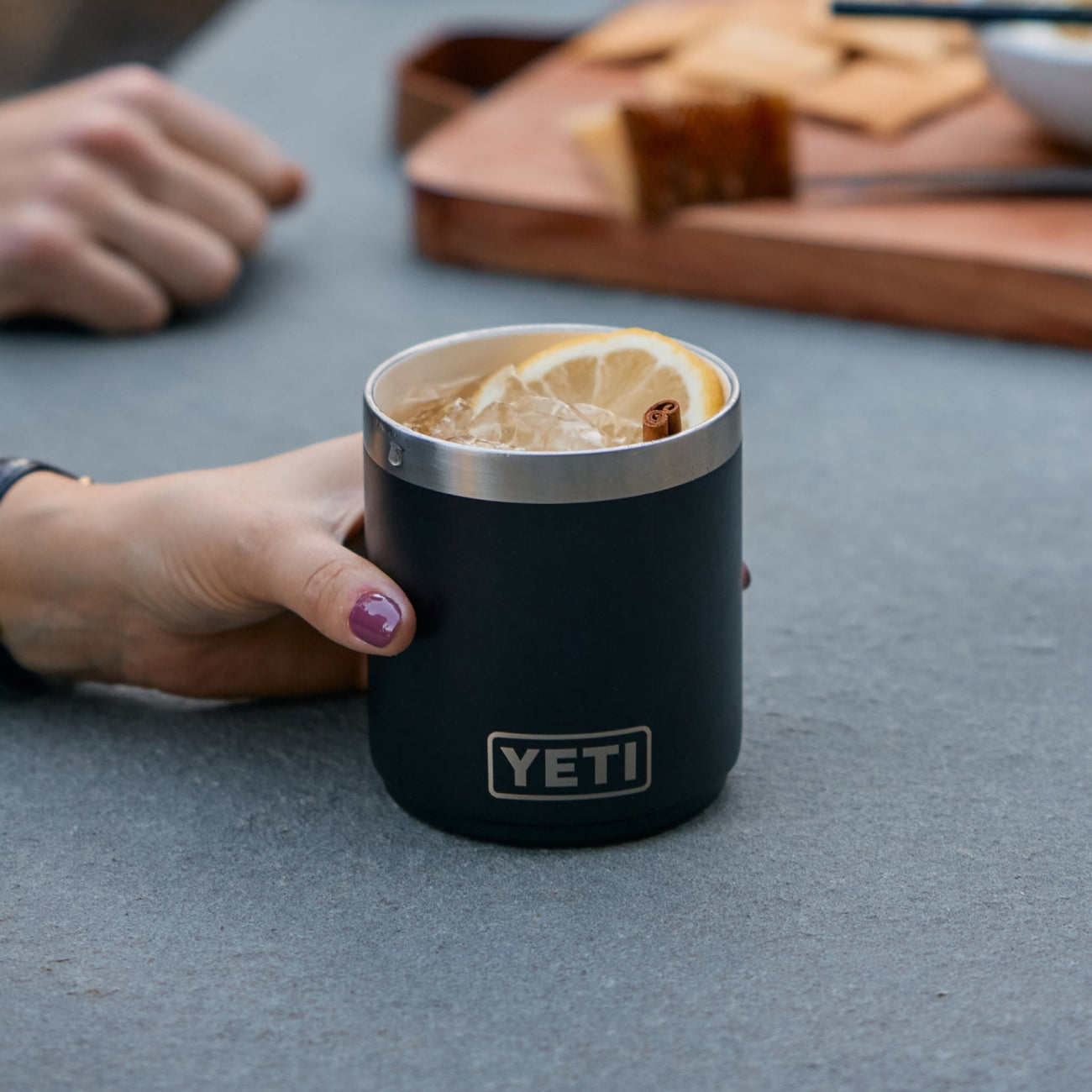 Person holding a YETI lowball with a drink on a table
