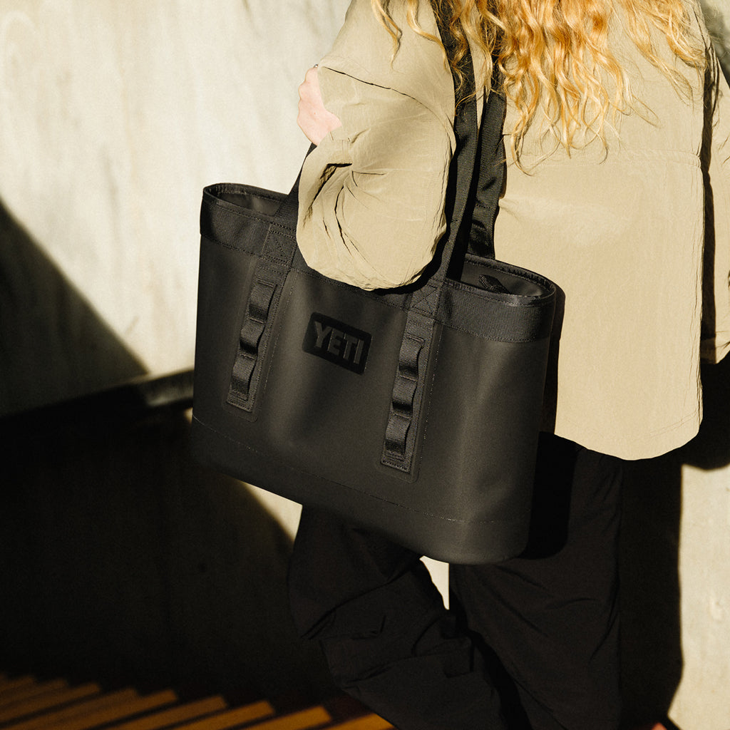 Person holding a black YETI camino tote bag against a neutral background