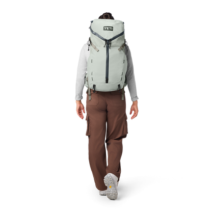 Person wearing a large backpack with 'YETI' branding on a white background