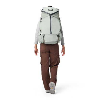 Person wearing a large green backpack with YETI logo on a white background